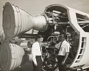 photo of John (left) standing in front of an Apollo capsule