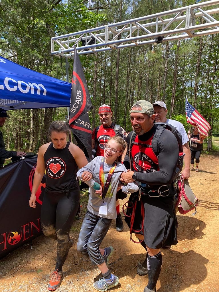 photo of Dave helping an obstacle course runner with More Heart Than Scars