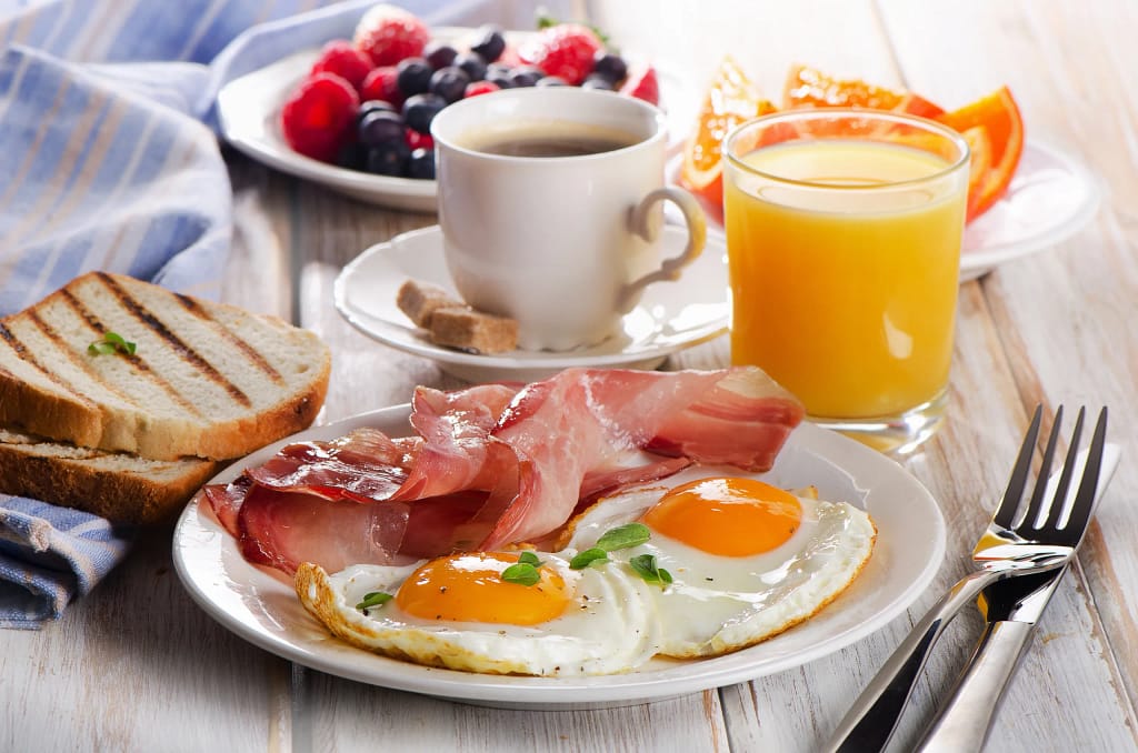 Breakfast of eggs, bacon, toast, berries, coffee and orange juice