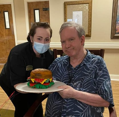 photo of Alicia Allmon with resident Stephen McCarty and his burger cake