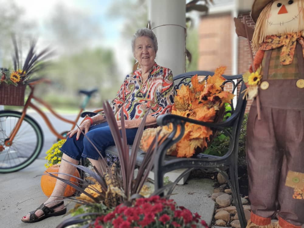 Senior lady sitting on a bench outside surrounded by fall decorations