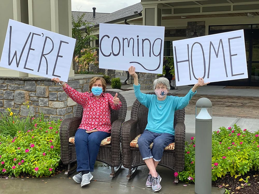 Two senior ladies holding signs that read "We're Coming Home"